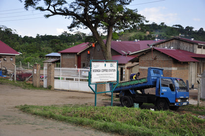Blue truck parked in front of a building with a signboard labeled 'Kisinga Coffee Station'.