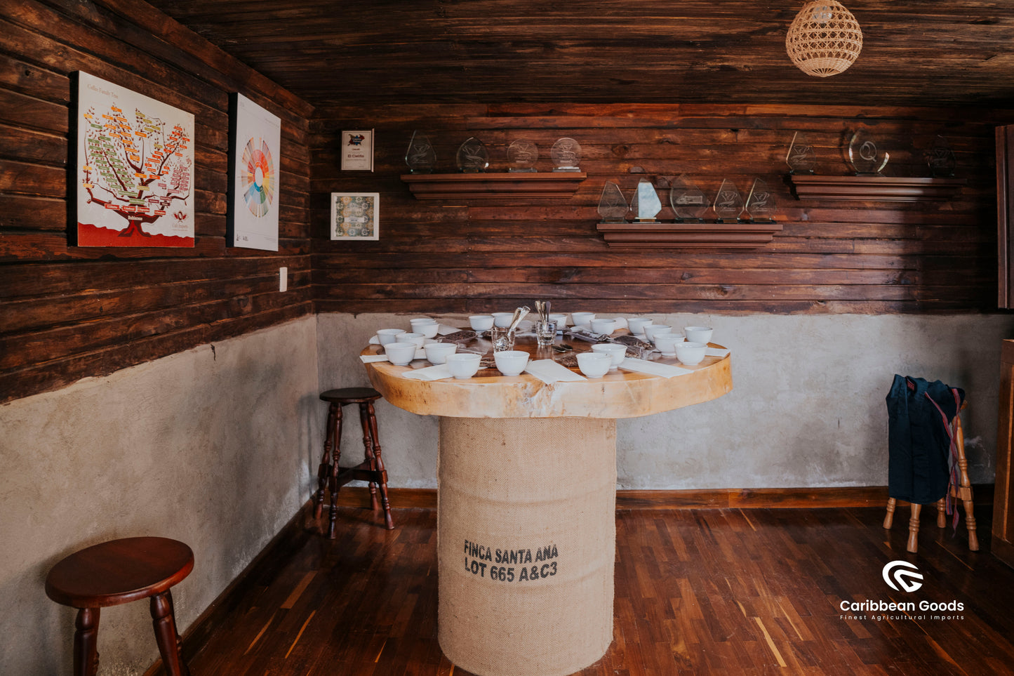 Wooden barrel table with coffee cupping setup laid out in a rustic room with wooden walls and floor. Shelves in the walls are full of awards.