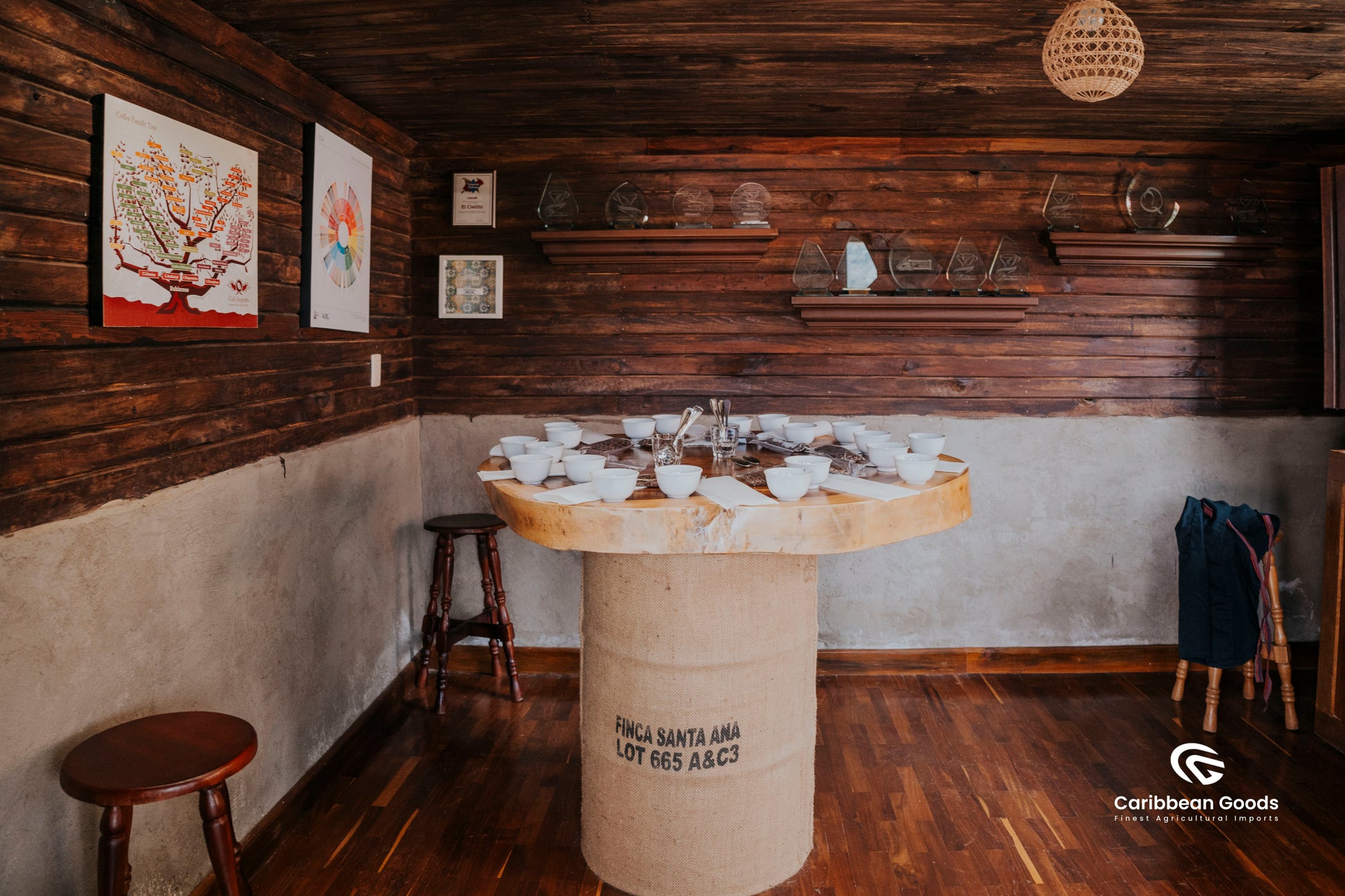 Wooden barrel table with coffee cupping setup laid out in a rustic room with wooden walls and floor. Shelves in the walls are full of awards.