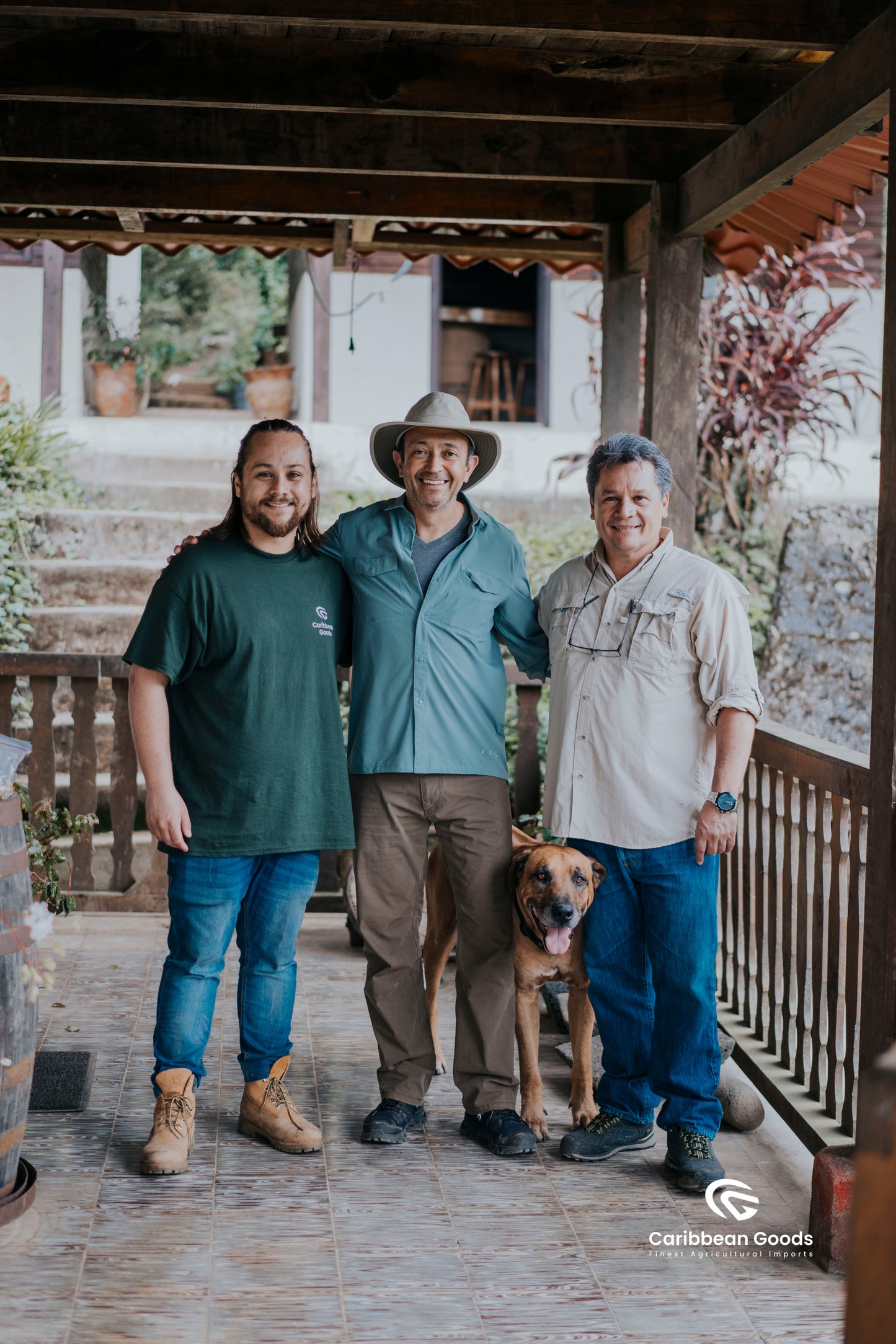 Three men standing on a wooden porch with a dog, wearing casual clothing.