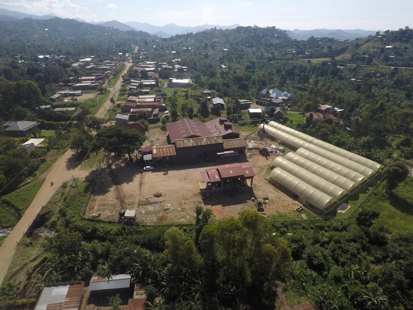 Aerial view of a village with houses and green fields in a hilly area.