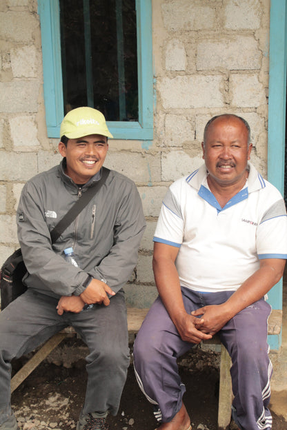 Two men sitting on a bench outside a building with a stone wall.